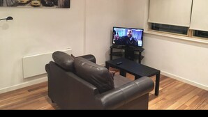 Un salon avec un canapé en cuir noir, un téléviseur à écran plat et un tableau représentant New York accroché au mur.