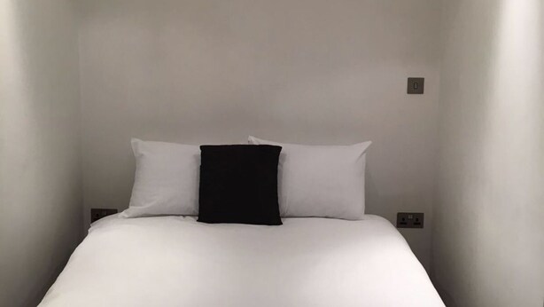 A small, narrow hotel room with a single bed, white walls, and a ceiling light. - The Greengate Apartment (Salford)