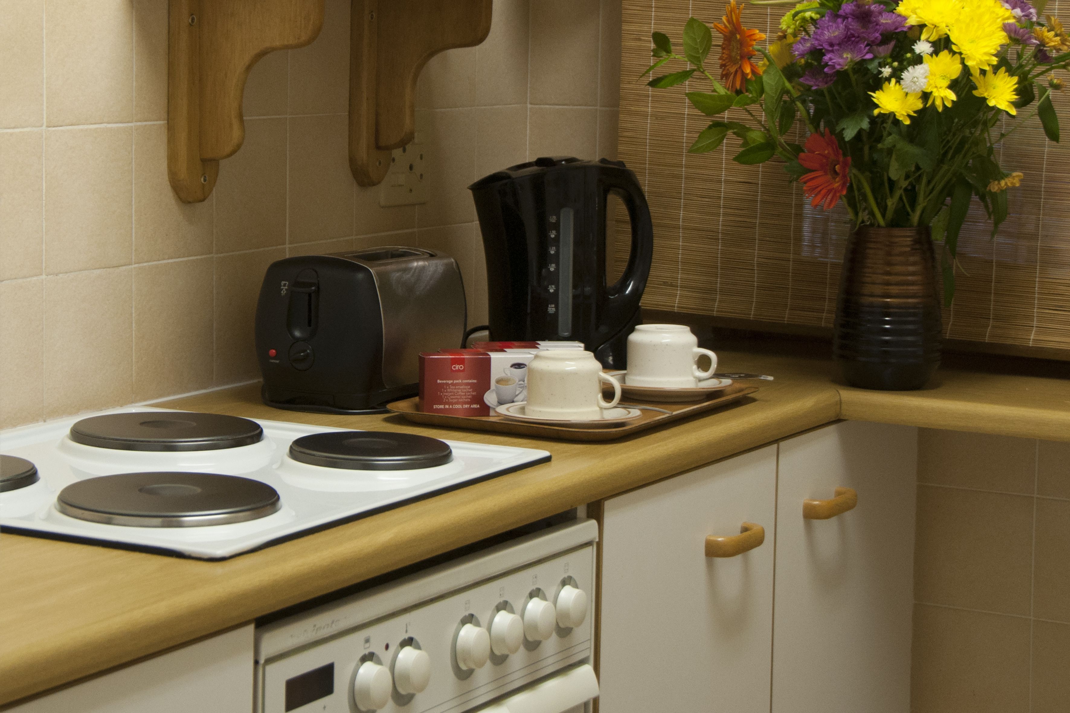 A kitchen with a stove, toaster, coffee maker, and a vase with flowers on the counter.