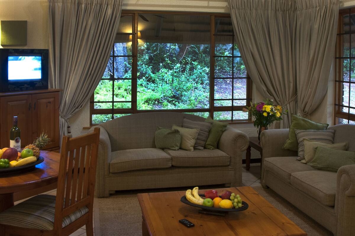 A living room with a sofa, a coffee table with fruit, a TV, and a window with curtains.