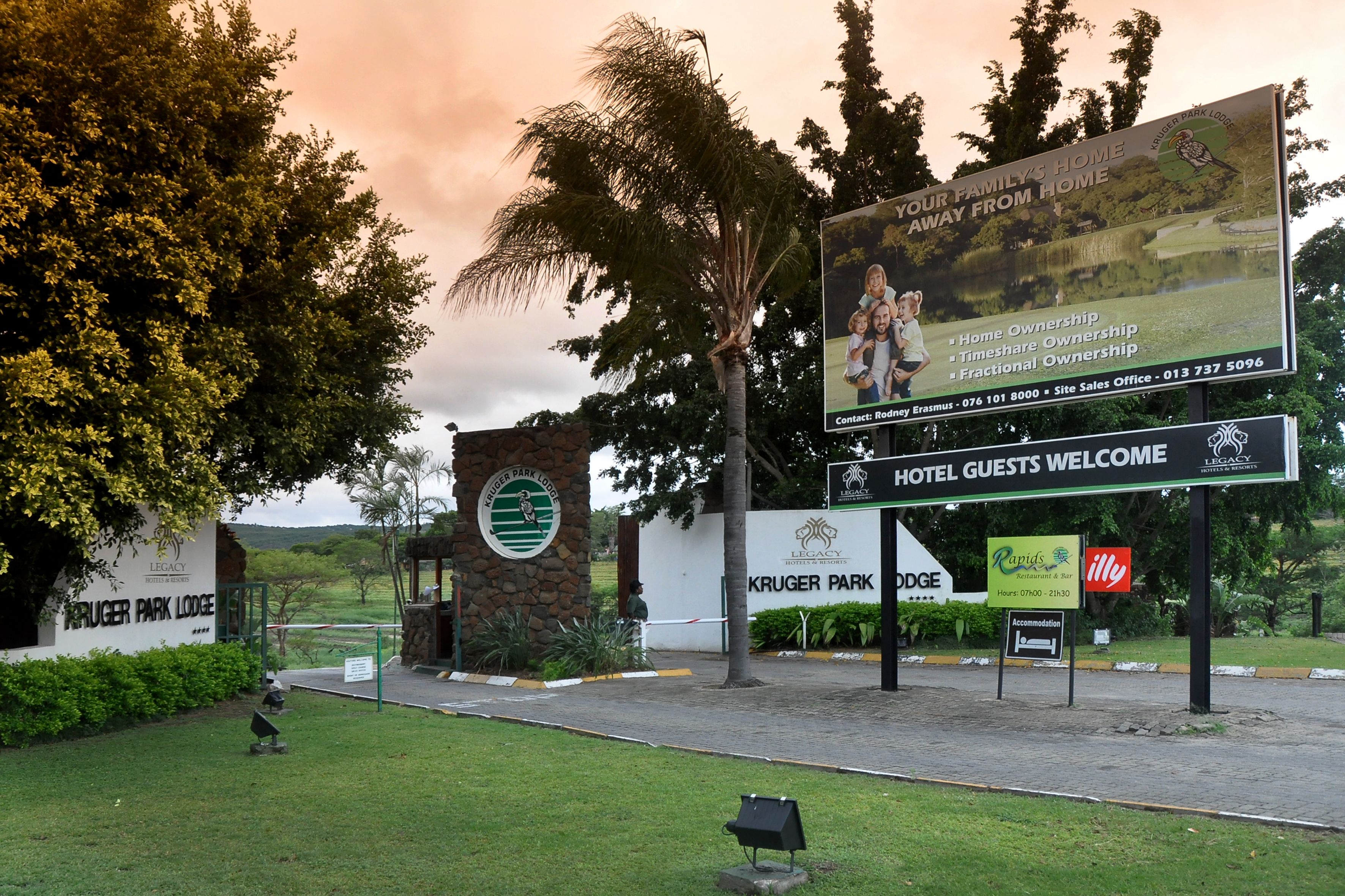 Entrada de un hotel con letrero de Kruger Park Lodge, un cartel de bienvenida y un letrero para el restaurante y bar Radis.