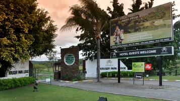 Entrada de un hotel con letrero de Kruger Park Lodge, un cartel de bienvenida y un letrero para el restaurante y bar Radis.