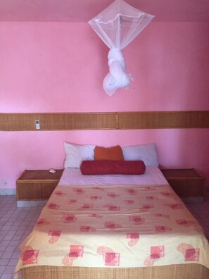 A bedroom with a bed, a bedside table, a nightstand, and a mosquito net. - Cocobay Saly (Mbour)