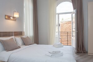 A hotel room with a bed, a wall-mounted light fixture, and a view of a brick building through an open door. - Hotel Casa Calda (Kutaisi)