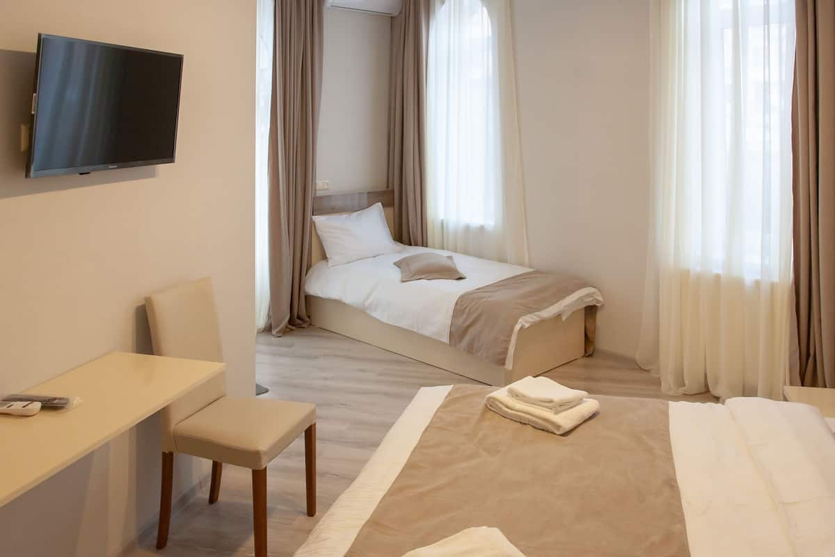 A hotel room with a bed, a desk, a chair, a TV, and curtains.