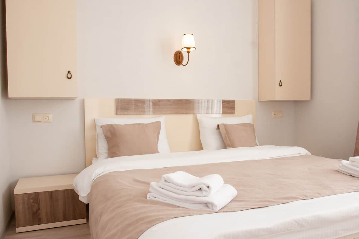 A neatly made bed with a beige and white duvet, a wooden nightstand, and a wall-mounted light fixture.