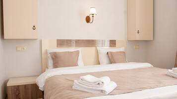 Una cama bien hecha con edredón beige y blanco, una mesita de noche de madera y una lámpara de pared.