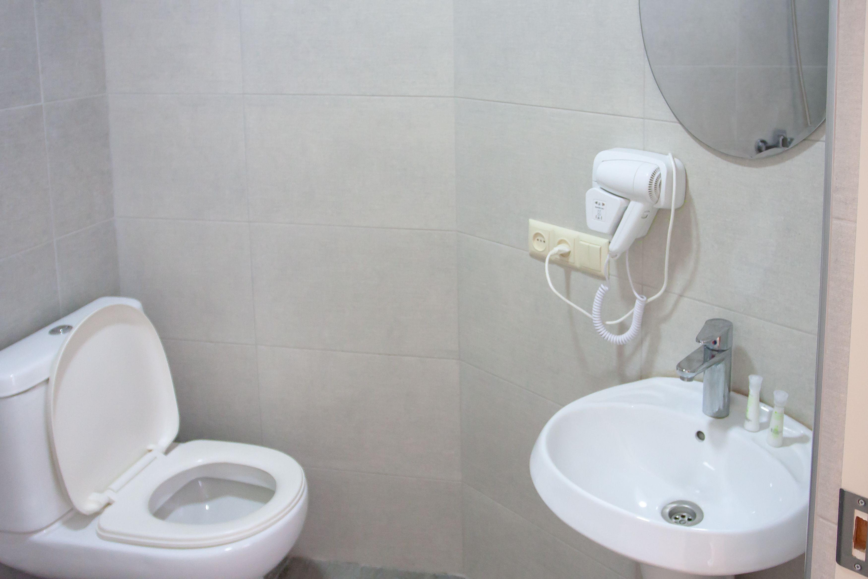 A bathroom with a toilet, a sink, and a hairdryer mounted on the wall.