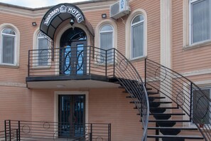 A hotel with a sign above the entrance, a balcony with a railing, and a spiral staircase leading to the entrance. - Hotel Casa Calda (Kutaisi)