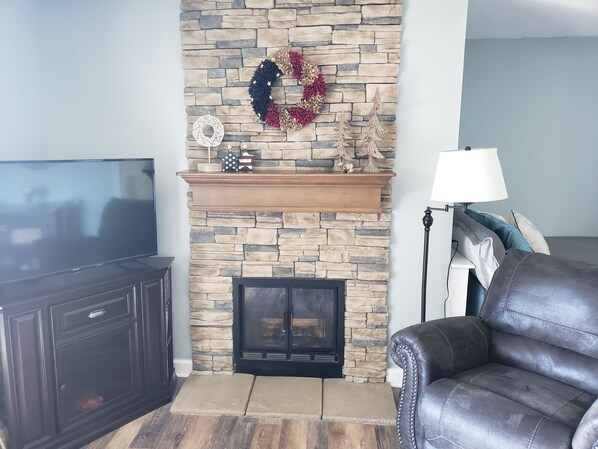 Una sala de estar con chimenea de piedra, televisor, sofá de cuero y lámpara.