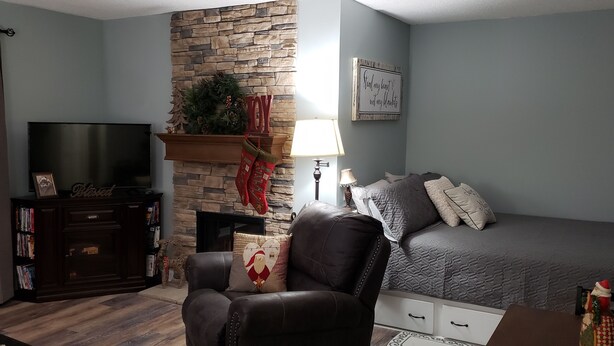 A cozy living room with a stone fireplace, a comfortable sofa, a flat-screen TV, and a bookshelf. - Studio with Breathtaking Mountain View (Gatlinburg)