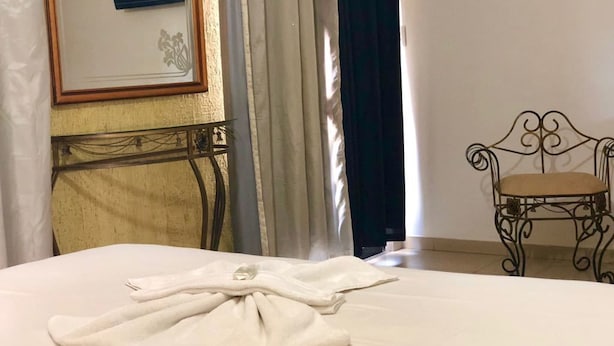 Una cama bien hecha con una toalla doblada, un cuadro en la pared y una silla metálica con cojín.