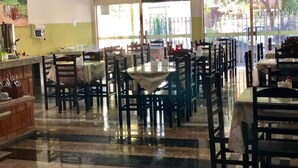 Un amplio comedor de hotel con varias mesas y sillas, una zona de cocina con equipo de cocina y ventanas grandes que ofrecen vistas al exterior.