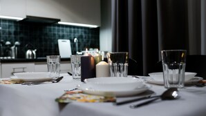 A dining table set with plates, glasses, and candles, with a modern kitchen in the background. - Crystal Apartments (Warsaw)