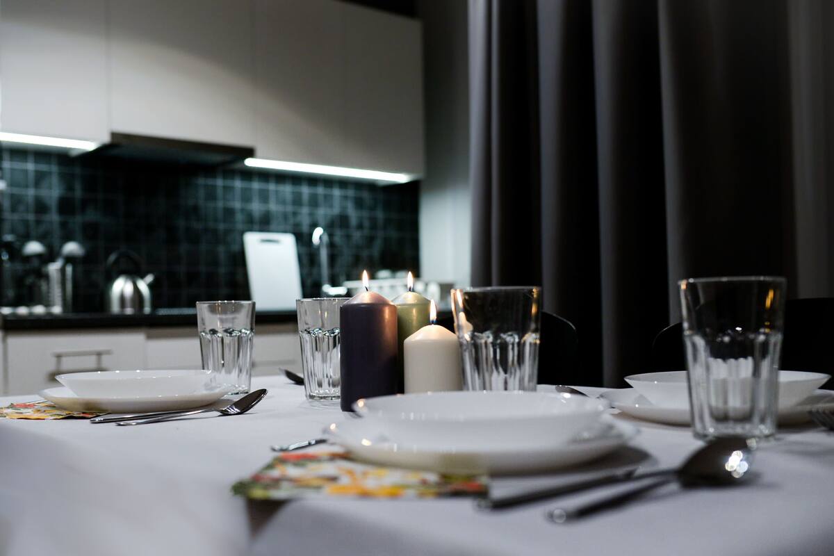 A dining table set with plates, glasses, and candles, with a modern kitchen in the background.