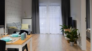 A modern living room with a dining area, featuring a sofa, a TV, and potted plants. - Crystal Apartments (Warsaw)