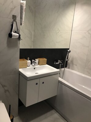 Un baño con lavamanos blanco, un espejo, toallero, ducha y retrete.