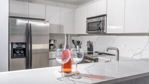 Una cuina moderna amb encimera de marbre blanc, electrodomèstics d'acer inoxidable i una ampolla de vi.