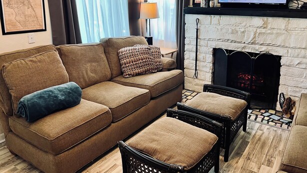 A living room with a brown sofa, two armchairs, a TV on a mantel, a fireplace, and a map on the wall. - At the Center of it All! (Titusville)