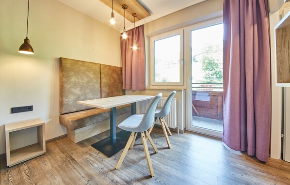 A modern dining area with a wooden table, two grey chairs, a bench, and a view through a large window with purple curtains.
