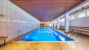 Piscina interna com piso de azulejos, bancos e teto de madeira.