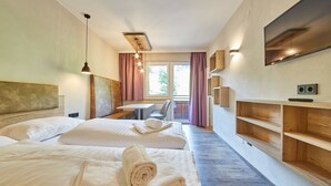 Quarto de hotel com duas camas, uma escrivaninha, uma cadeira, uma televisão e prateleiras embutidas.