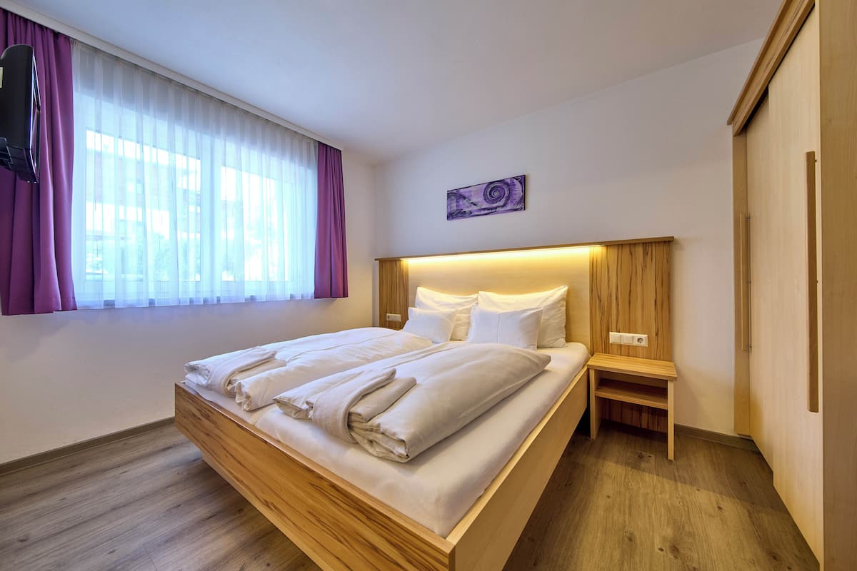 Cama bem arrumada com cabeceira de madeira, mesa de cabeceira e janela com cortinas.