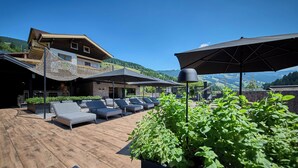 A rooftop lounge with sun loungers and umbrellas, overlooking a mountainous landscape. - ThePoolhouse Boutique Lodge (Saalbach-Hinterglemm)