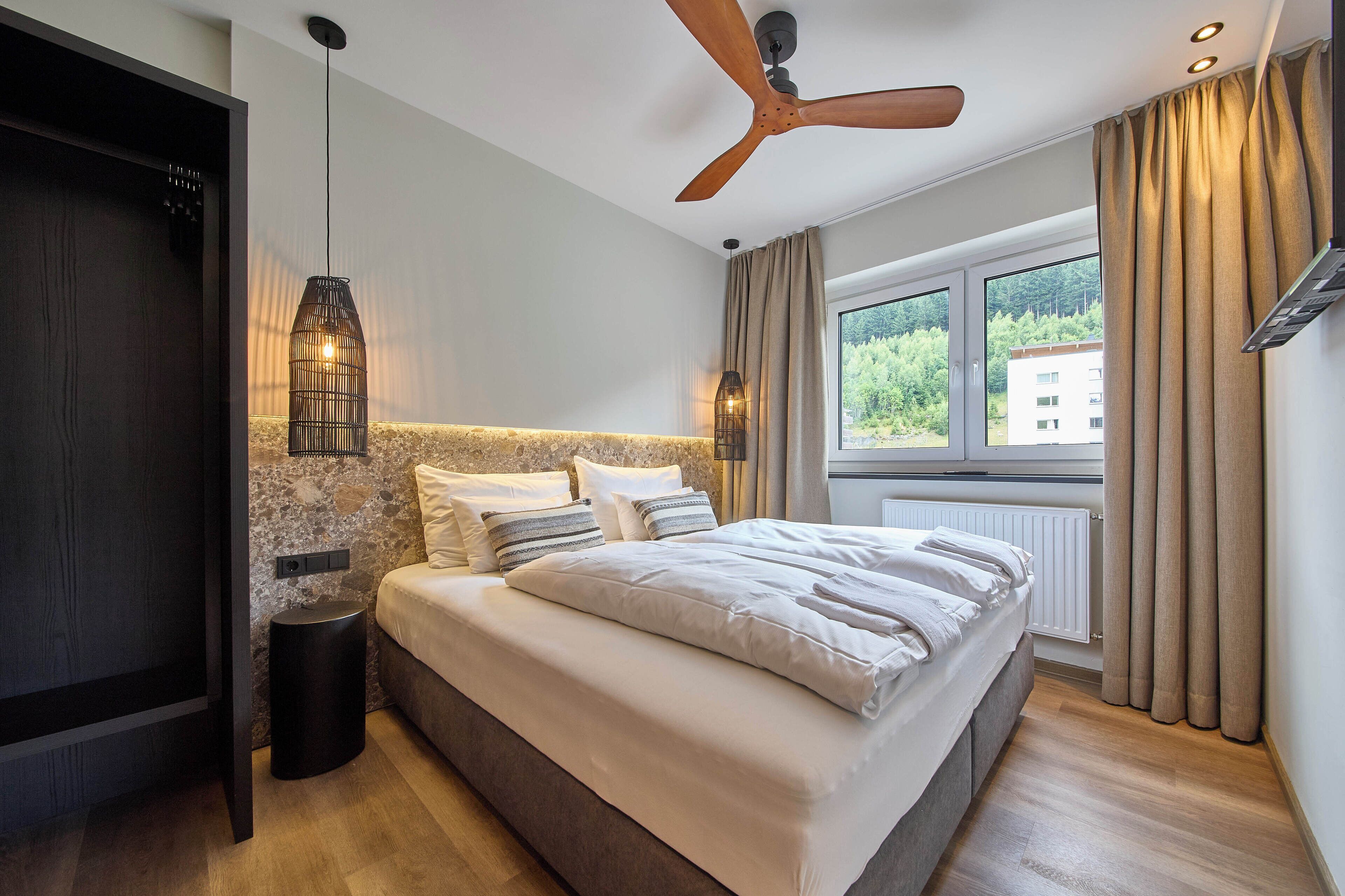 Een moderne slaapkamer met een groot bed, een plafondventilator, een accentmuur van steen en een raam met gordijnen.