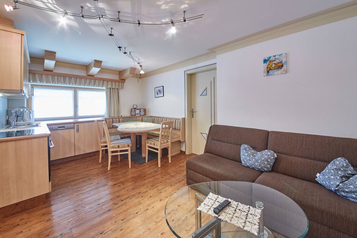 Uma sala de estar moderna com um sofá marrom, mesa de centro de vidro e piso de madeira.