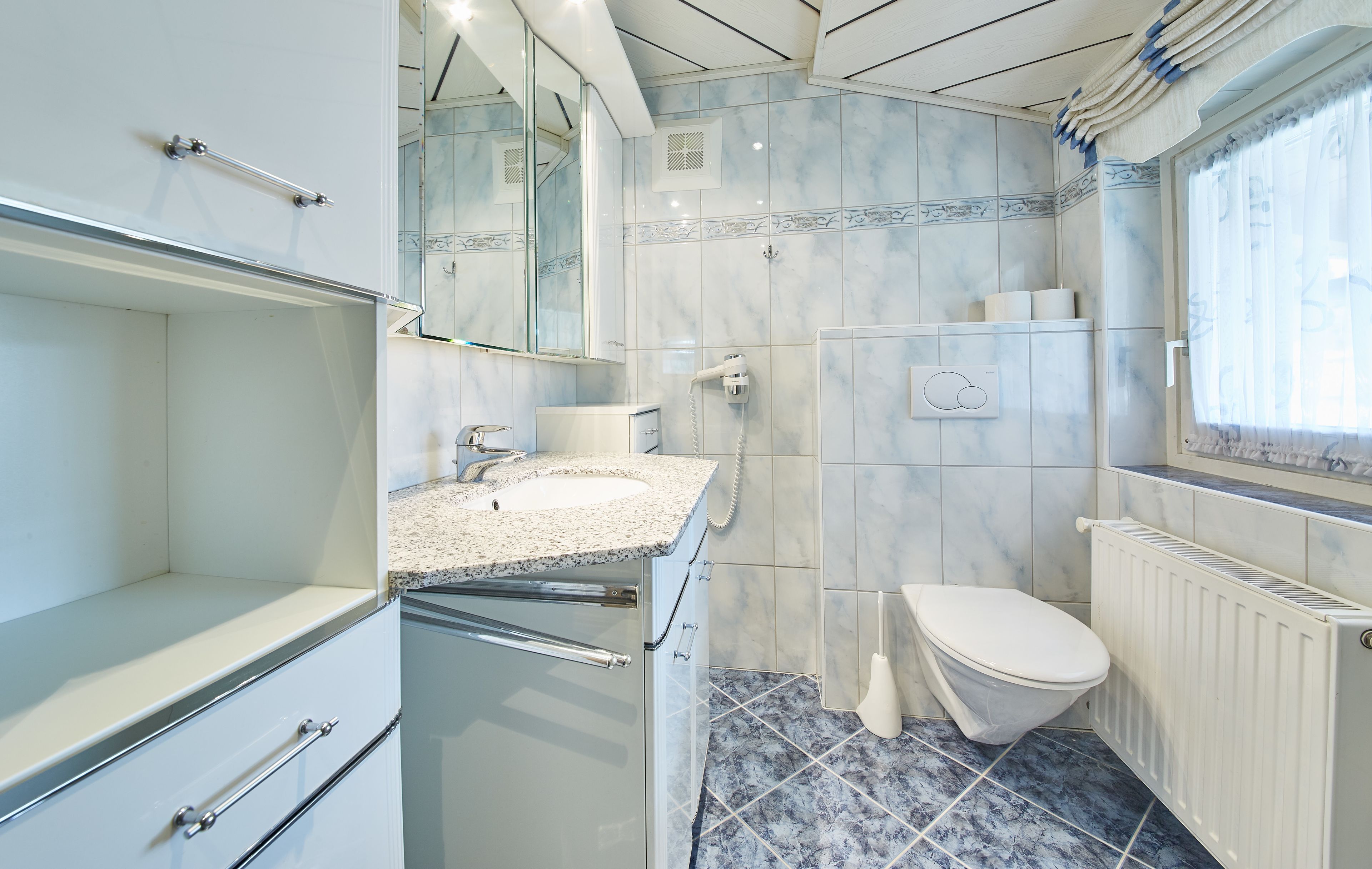 A bathroom with a marble floor, a white toilet, a sink with a mirror, and a shower area.