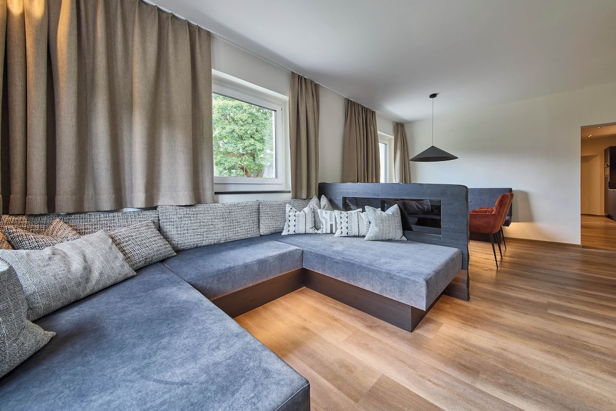 Uma sala de estar moderna com sofá em formato de L, lareira e área de jantar.