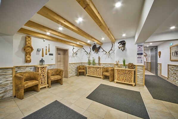 A lobby with wooden beams, stone walls, and antler decorations. There are plush chairs and a reception desk.