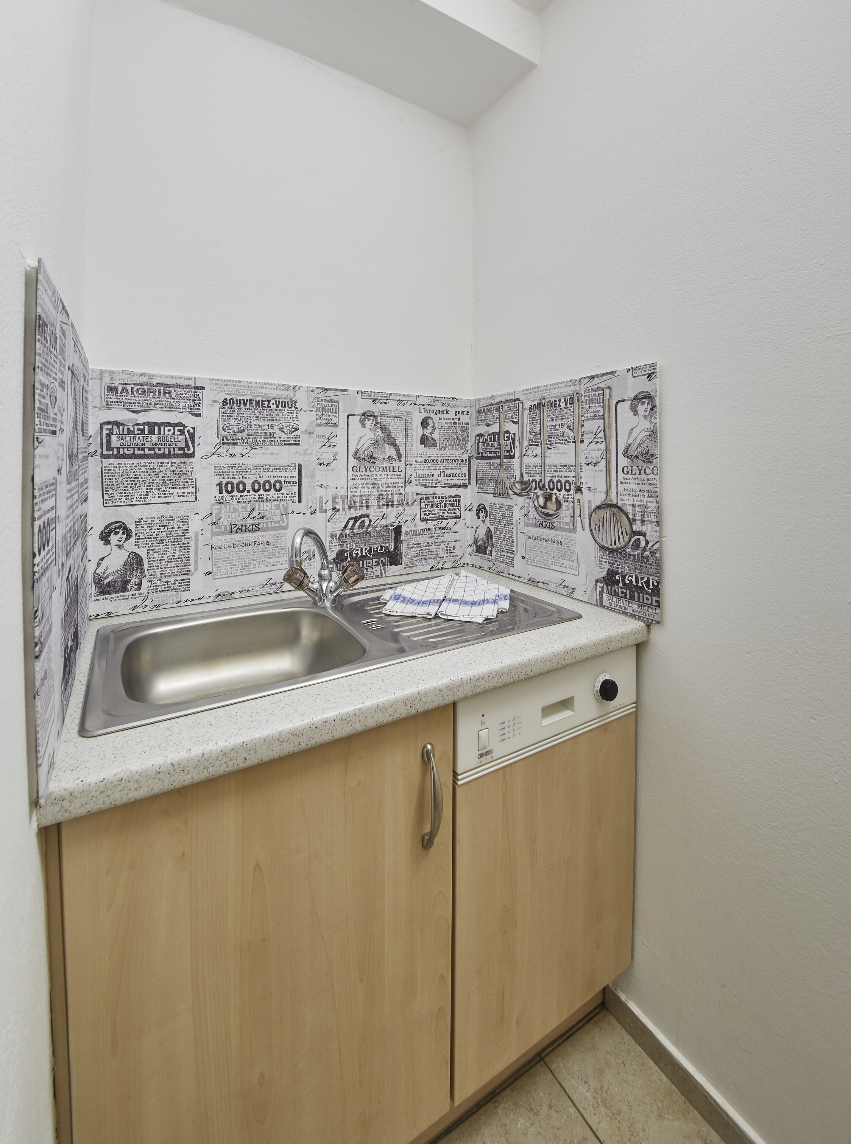 A kitchen with a sink, wooden cabinets, and a backsplash covered with newspaper clippings.