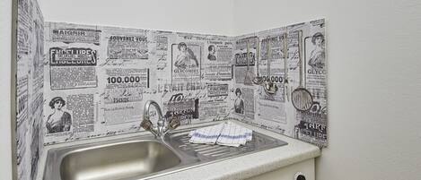 Une cuisine équipée d’un évier, de meubles de rangement en bois et d’un crédence recouverte de coupures de journaux.