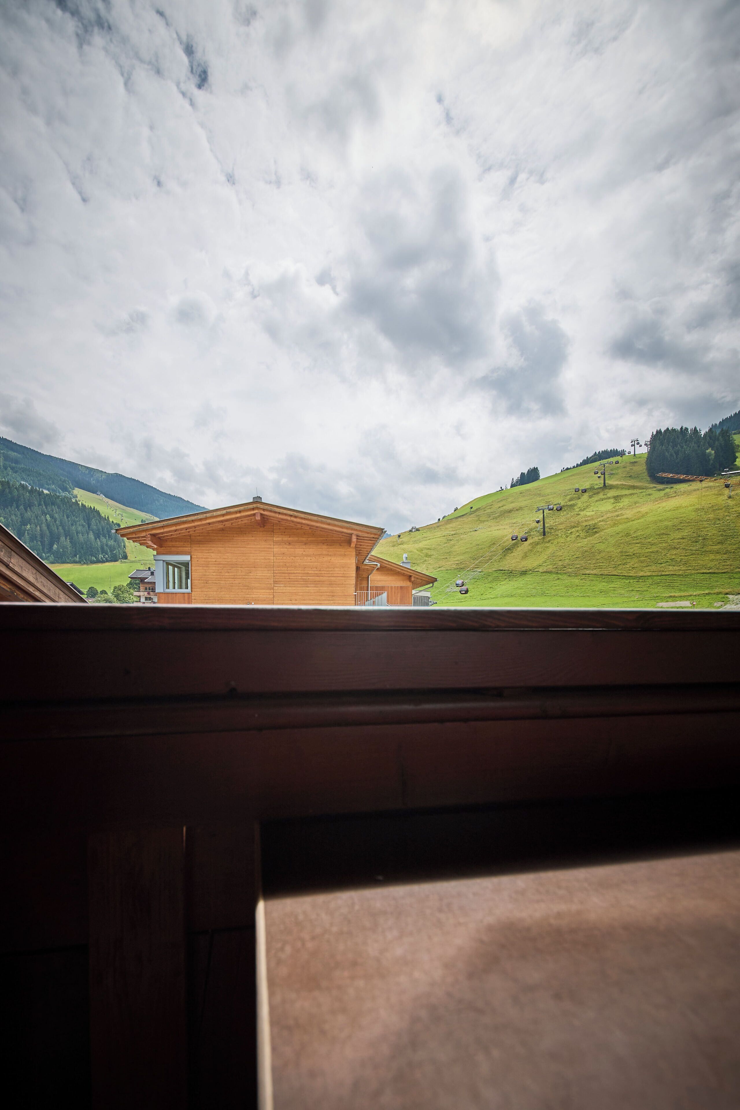 A wooden cabin with a view of a green hillside and a cloudy sky.