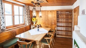 A wooden dining area with a large table, benches, and a shelf with glasses. - Chalet Appartement Alpenherz (Saalbach-Hinterglemm)