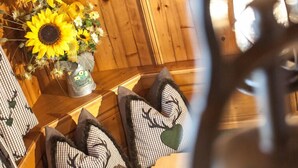 A wooden interior with a wooden wall, a table with a vase of sunflowers, and patterned cushions. - Chalet Appartement Alpenherz (Saalbach-Hinterglemm)