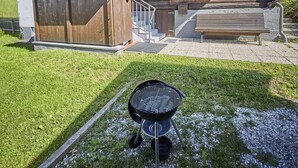 A wooden chalet with a stone staircase, a wooden bench, and a grill. - Chalet Appartement Alpenherz (Saalbach-Hinterglemm)
