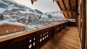 A wooden balcony with a view of a snow-covered town and mountains. - Chalet Guter Hirte (Saalbach-Hinterglemm)