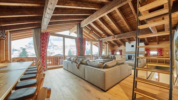 A spacious living area with a large sofa, wooden beams, and a view of a snowy landscape. - Chalet Guter Hirte (Saalbach-Hinterglemm)