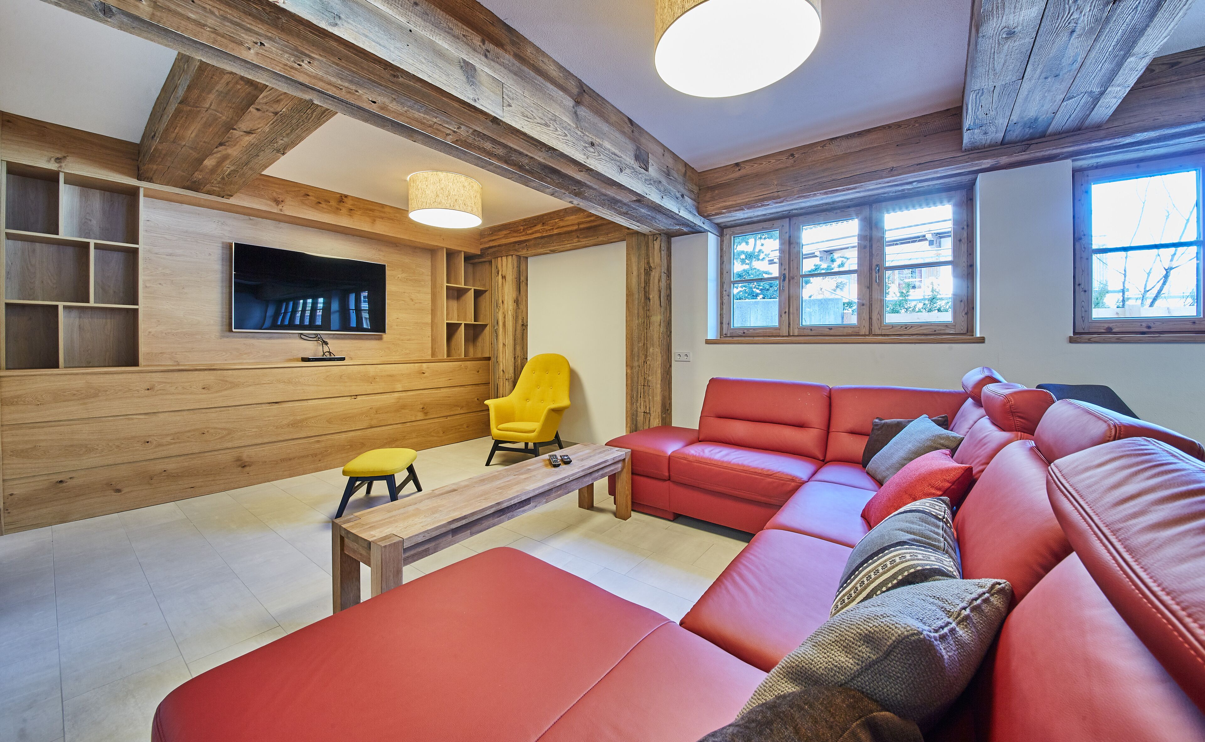 Ein gemütliches Wohnzimmer mit einem roten Sofa, einem gelben Sessel, Holzregalen und einem Fernseher.