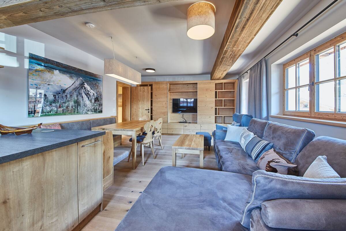 Een moderne woonkamer met een houten plafond, een groot schilderij, een televisie en een bank met kussens.