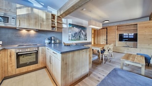 A modern kitchen with wooden cabinetry, a built-in oven, and a coffee maker. There is a dining area with a wooden table and chairs. - Chalet Guter Hirte (Saalbach-Hinterglemm)