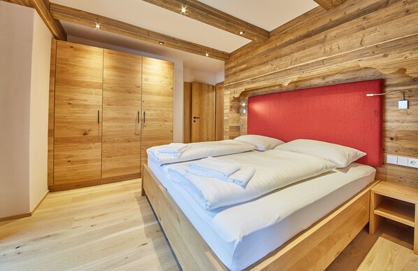 A bedroom with a wooden bed frame, a red headboard, and a wooden wardrobe. - Chalet Guter Hirte (Saalbach-Hinterglemm)