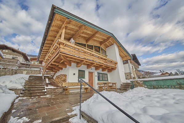 A wooden chalet with a balcony, stone steps, and a snow-covered ground. - D-Town Lodge (Saalbach-Hinterglemm)