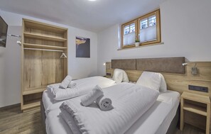 A bedroom with two beds, wooden wardrobe, and a window with blinds. - D-Town Lodge (Saalbach-Hinterglemm)