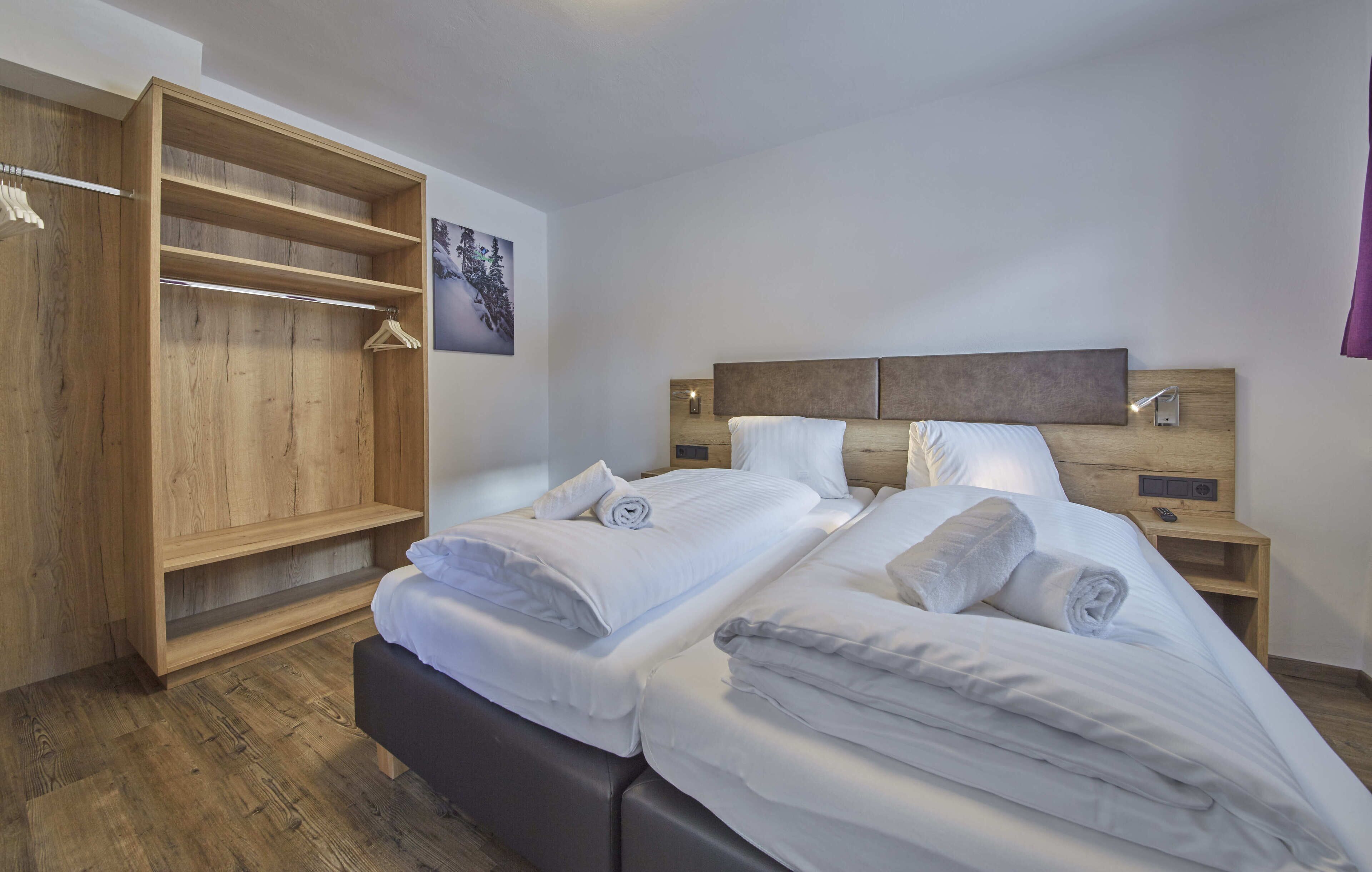 Une chambre d’hôtel avec deux lits, une armoire en bois et une table de chevet avec une lampe.