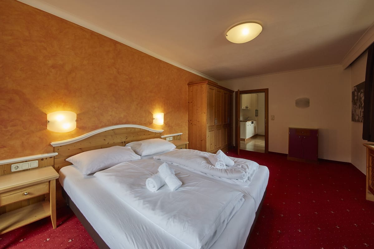Una habitación de hotel con una cama grande, dos mesitas de noche, un armario de madera y una alfombra roja.