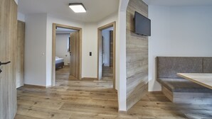 A modern interior with a wooden floor, a flat-screen TV mounted on a wall, and a bench. - Appartements Gappmaier (Saalbach-Hinterglemm)